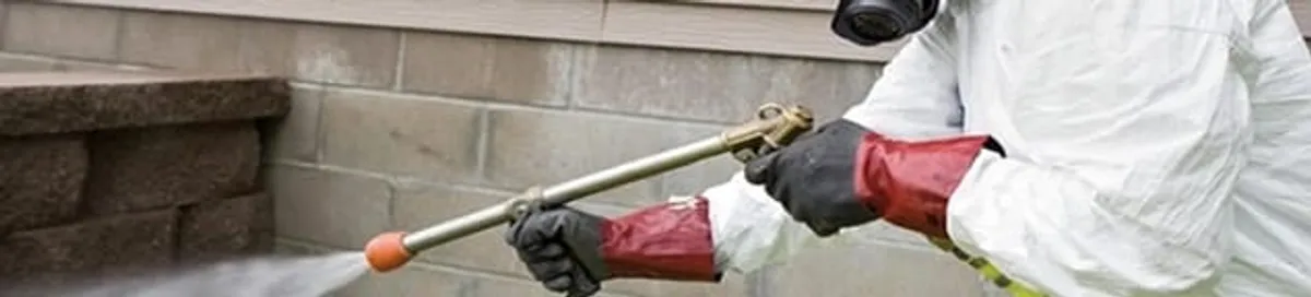 Pest control technician applying exterior insect treatment along a home foundation in Tucson, AZ