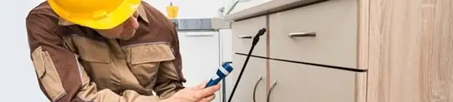 Roach exterminator applying treatment under kitchen cabinets in Tucson, AZ
