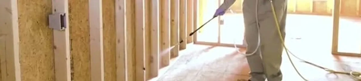 Termite treatment technician applying spray along framing and unfinished walls in Tucson, AZ