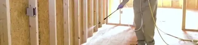 Termite treatment technician applying spray along framing and unfinished walls in Tucson, AZ
